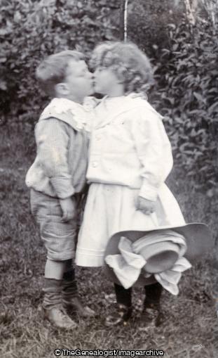 Children Kissing C1907 (1907, boy, Garden, Girl, hat, kissing)