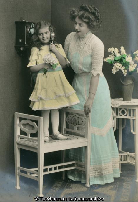 Mother and daughter in yellow standing on chair on phone C1900 (C1900, chair, daughter, flowers, Mother, pose, table, Telephone, vase)